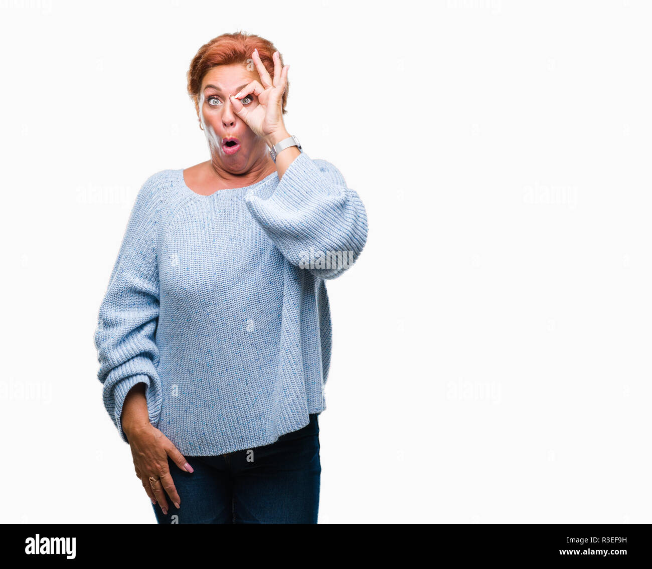 Atrractive senior caucasian redhead woman wearing winter sweater over isolated background doing ok gesture shocked with surprised face, eye looking th Stock Photo