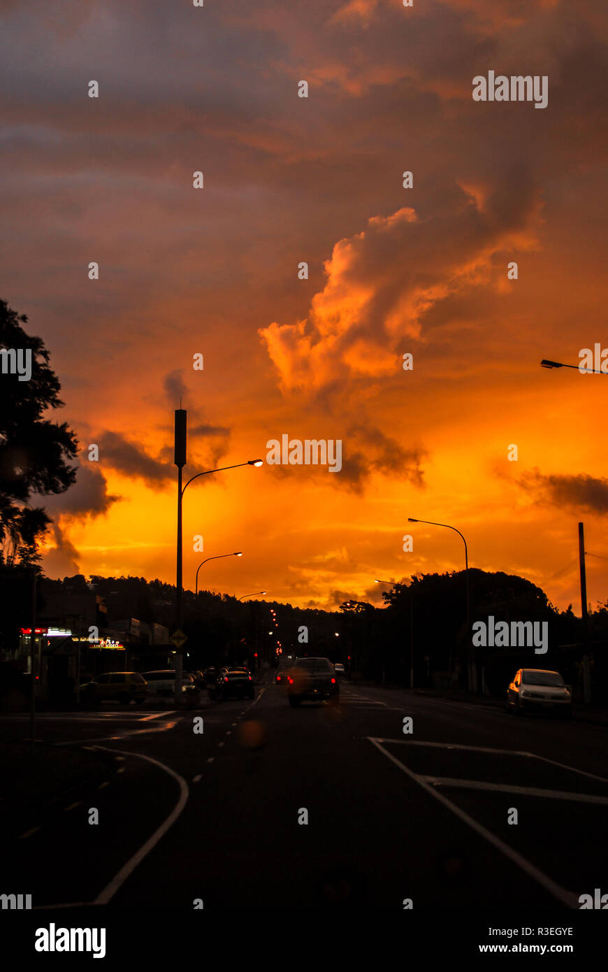 Driving on a road under a dramatic sunset in Green Bay, West Auckland, New Zealand Stock Photo