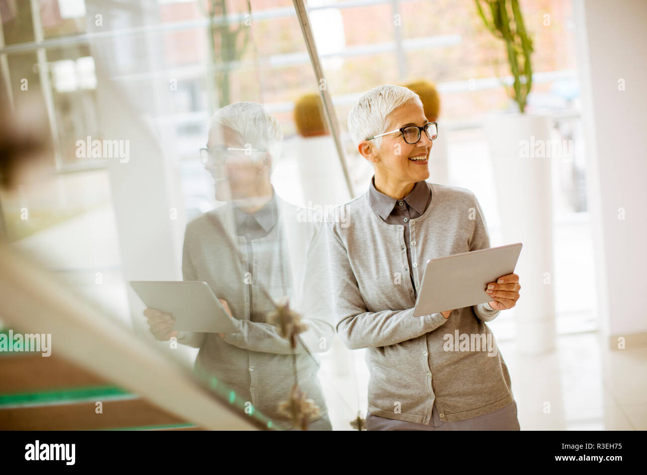 Pretty, positive, aged woman with beaming smile holding tablet in modern office Stock Photo