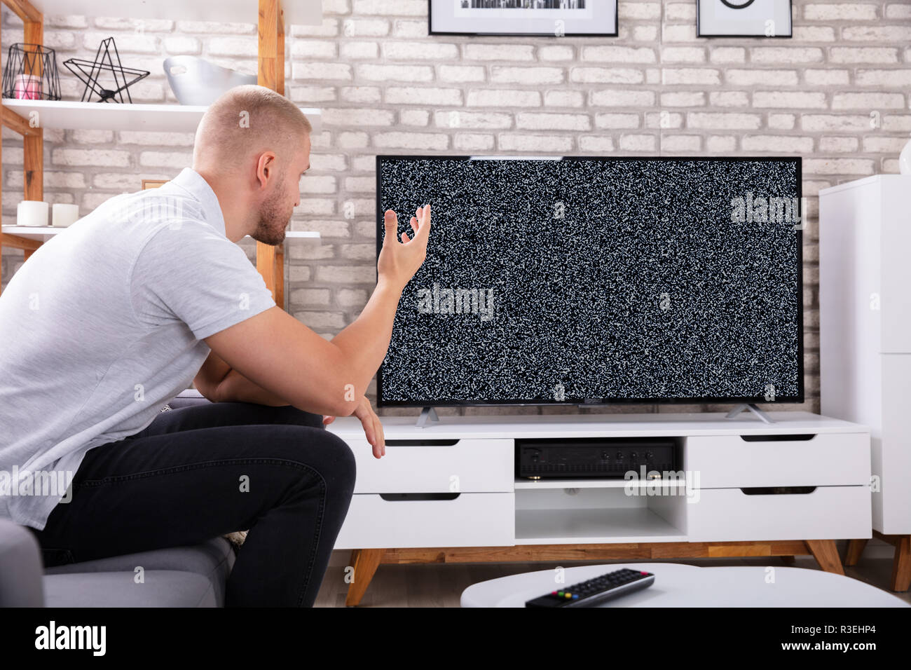 Frustrated Young Man Sitting On Sofa Near Television With No Signal Stock Photo
