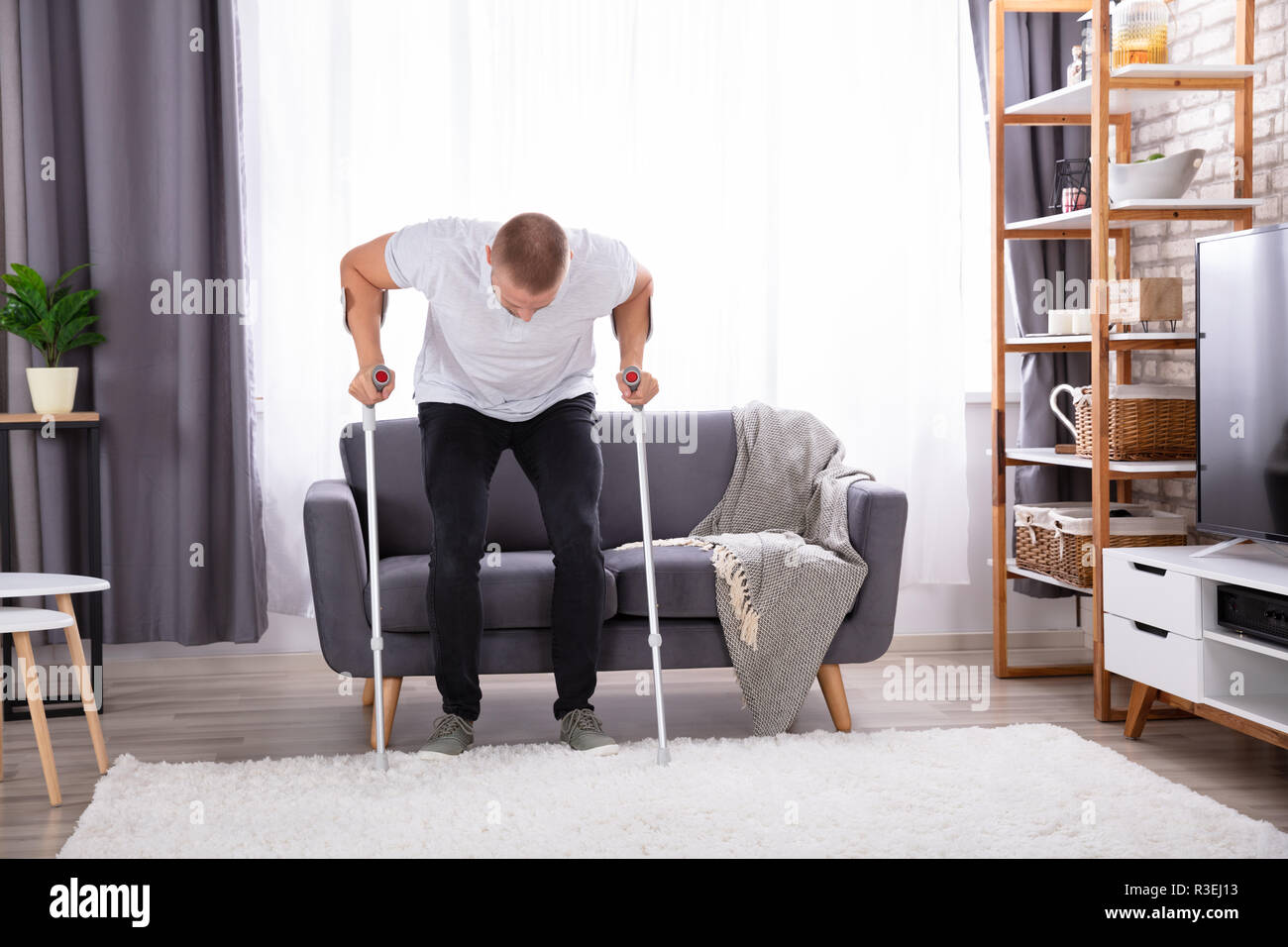 Disabled Young Man Using Crutches To Get Up From Sofa At Home Stock