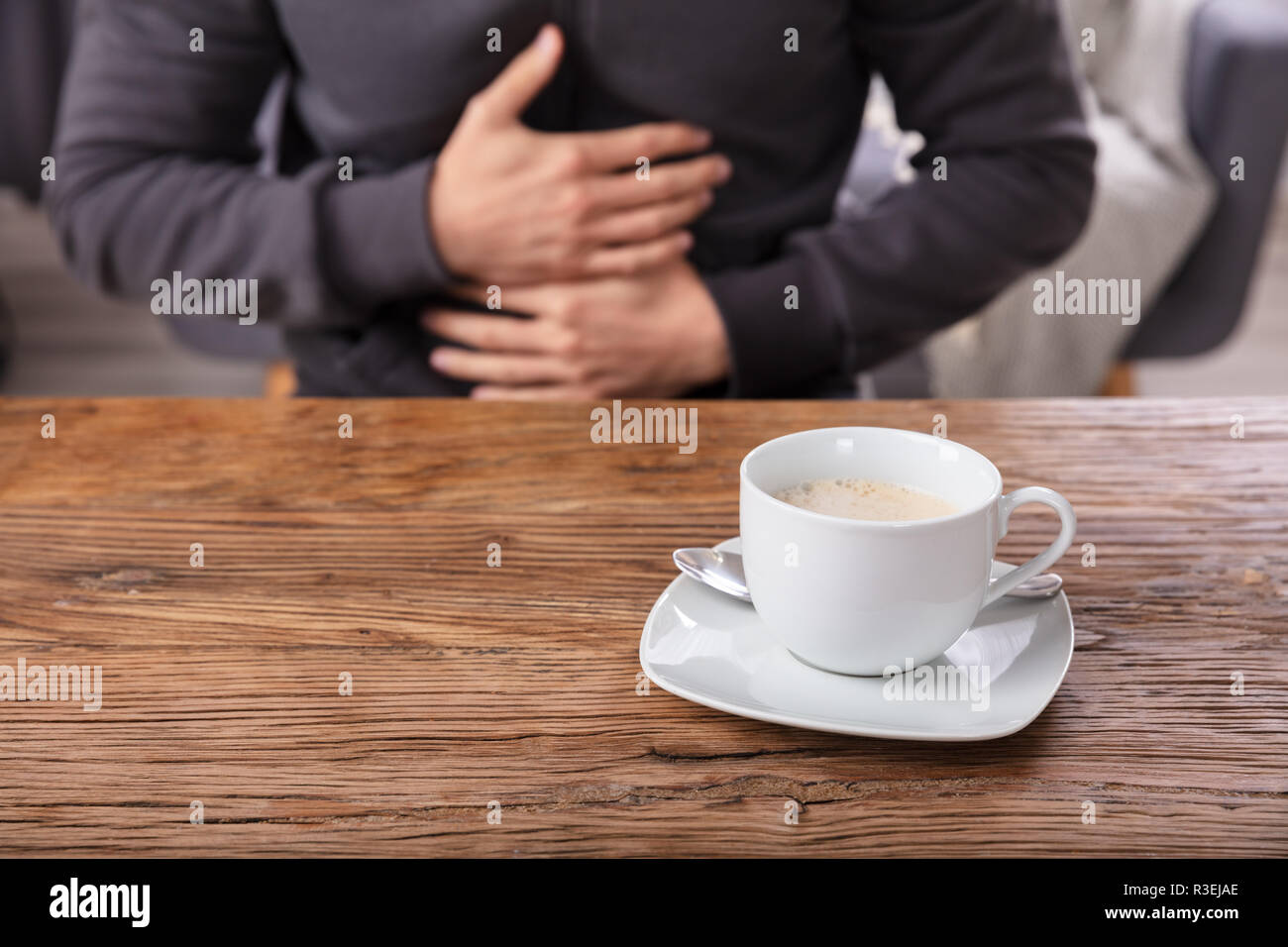 Man Suffering From Stomach Pain With Cup Of Coffee On Wooden Desk Stock