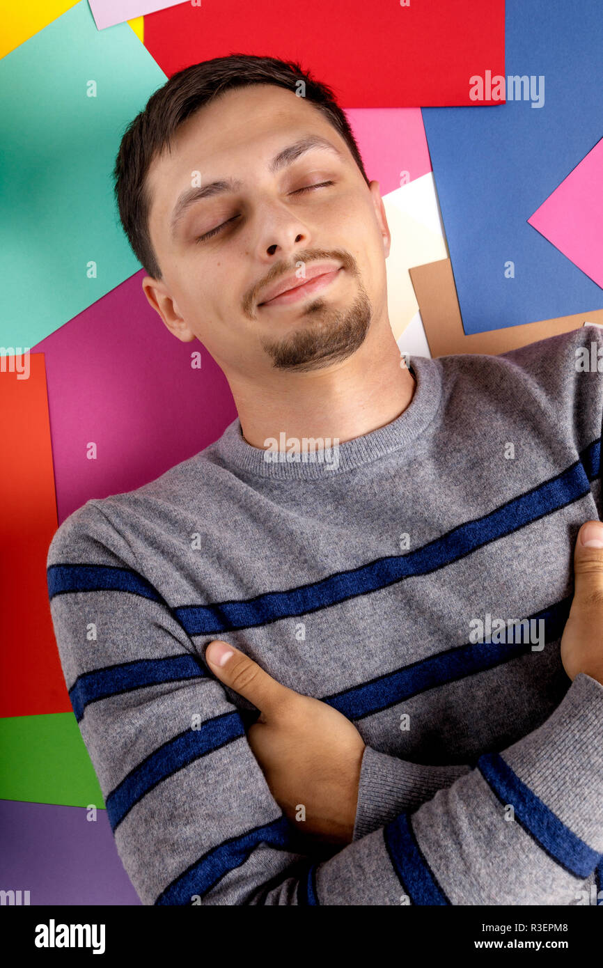 happy young man lying on multicolored paper sheets Stock Photo