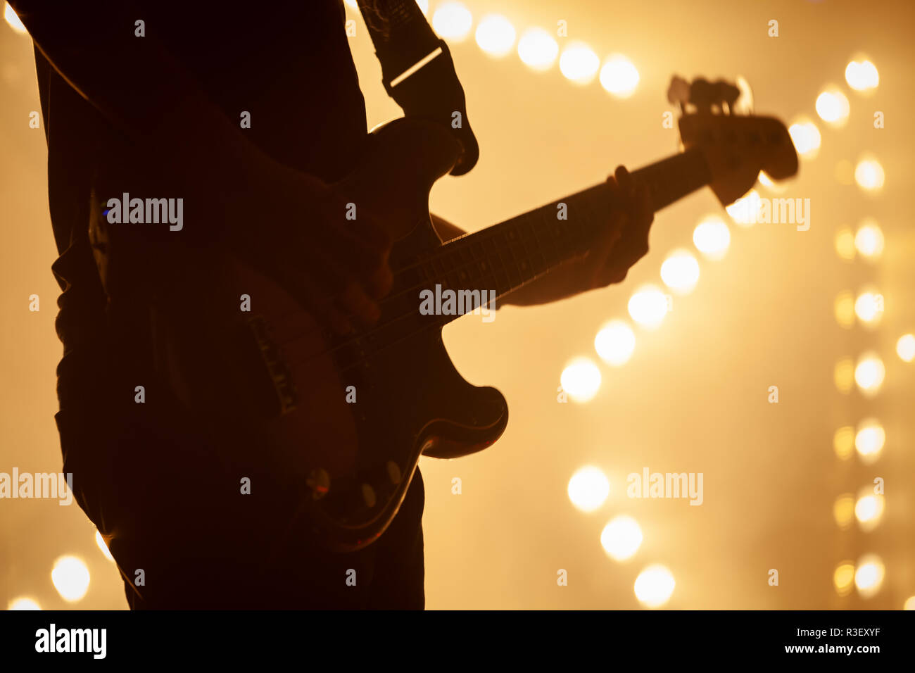 Electric bass guitar player in stage strobe lights, close-up silhouette photo with soft selective focus Stock Photo