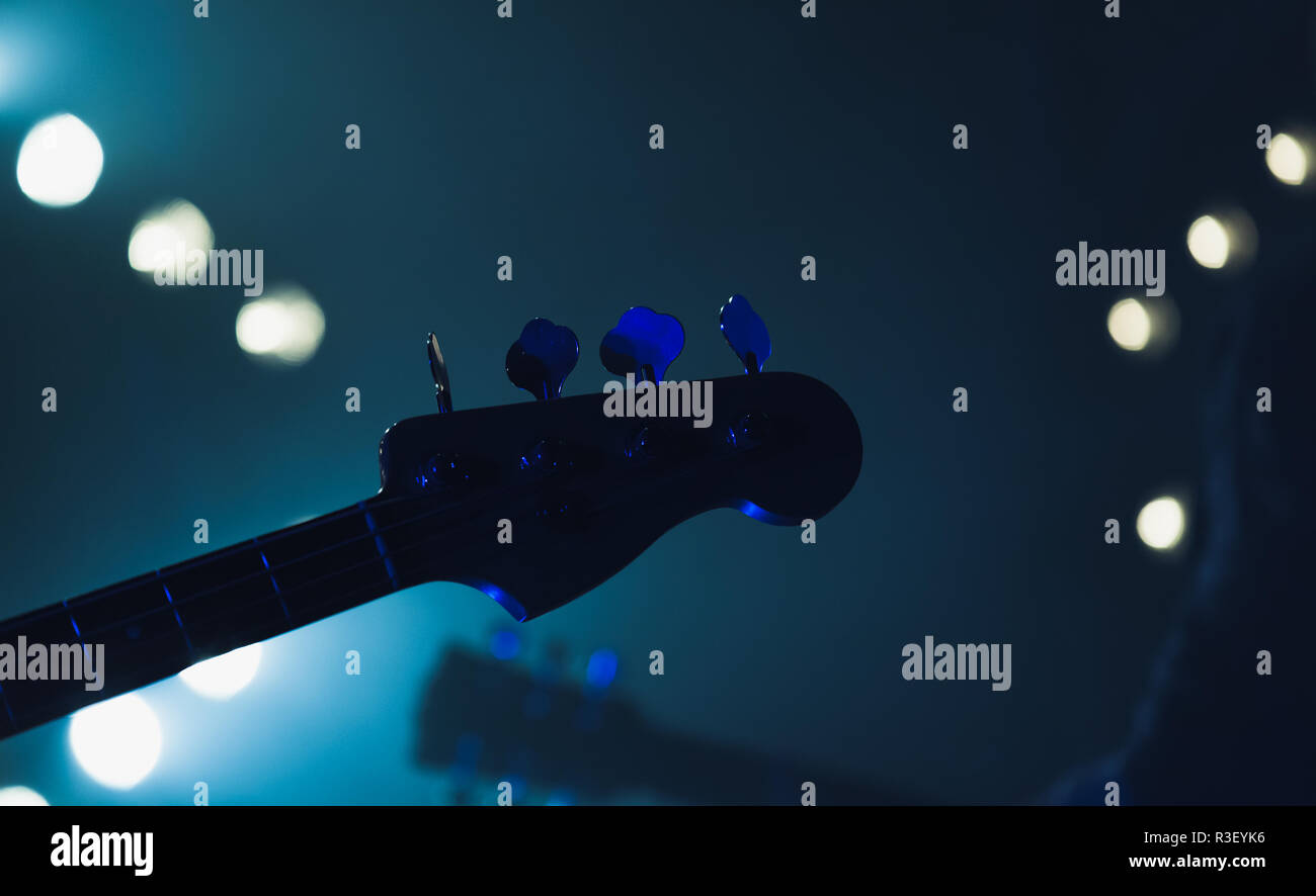 Live music background, electric bass guitar headstock silhouette in blue stage lights, close-up photo with soft selective focus Stock Photo