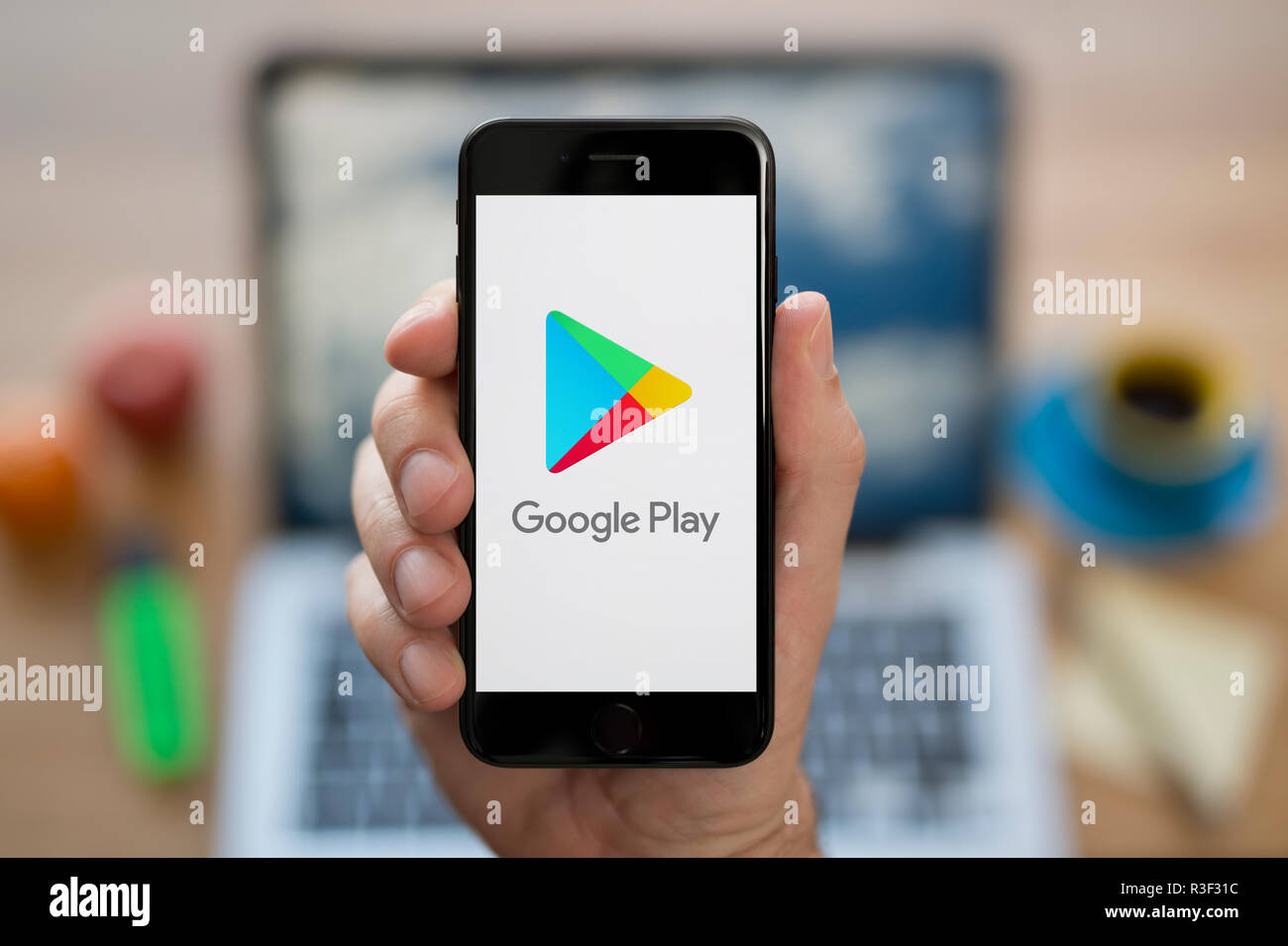 A man looks at his iPhone which displays the Google Play logo, while sat at  his computer desk (Editorial use only Stock Photo - Alamy