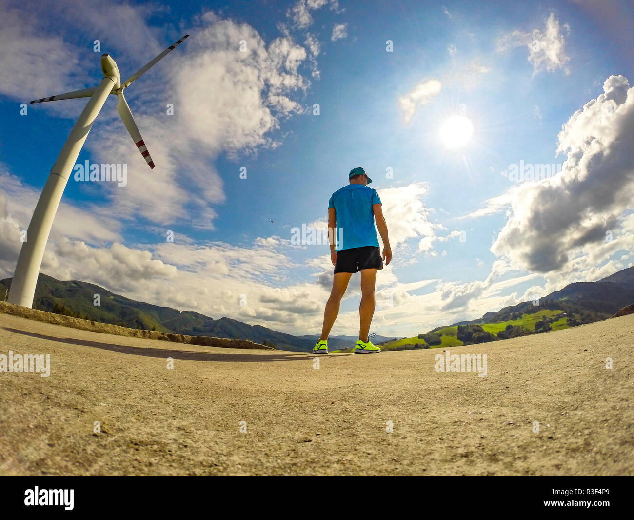 Male athlete runner standing at wind turbine and blue sky background ...
