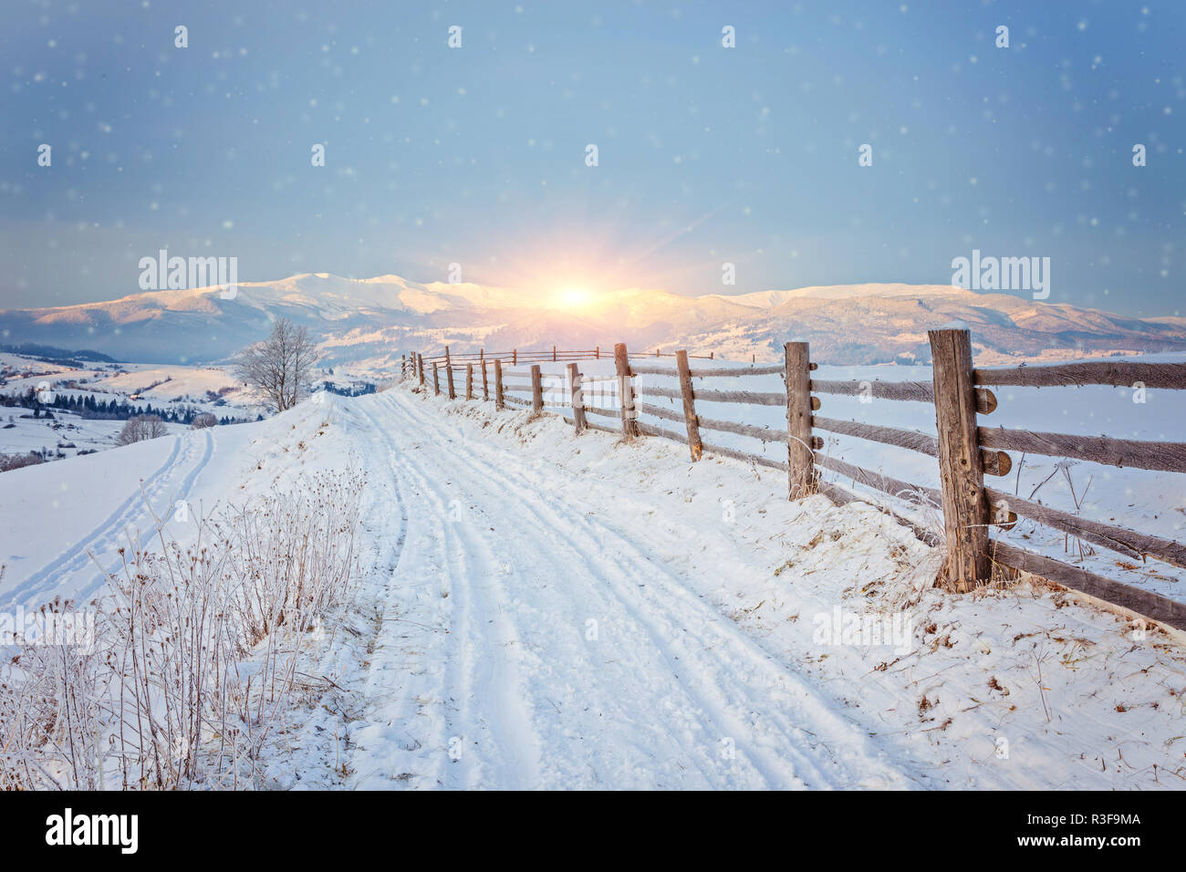 Winter country landscape with timber fence and snowy road into ...