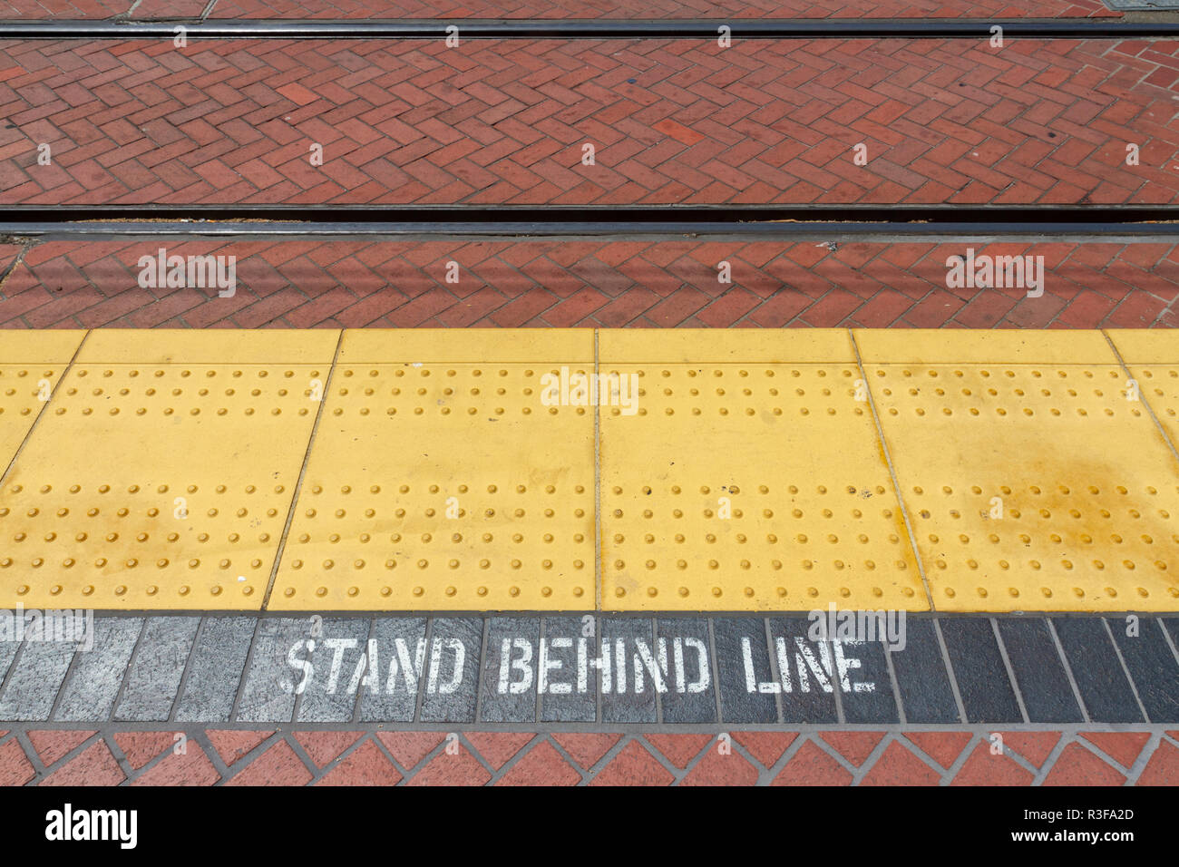 'Stand Behind Line' notice & dimpled yellow strip on the platform edge of a San Diego Trolley (train) system station, San Diego, CA, USA. Stock Photo
