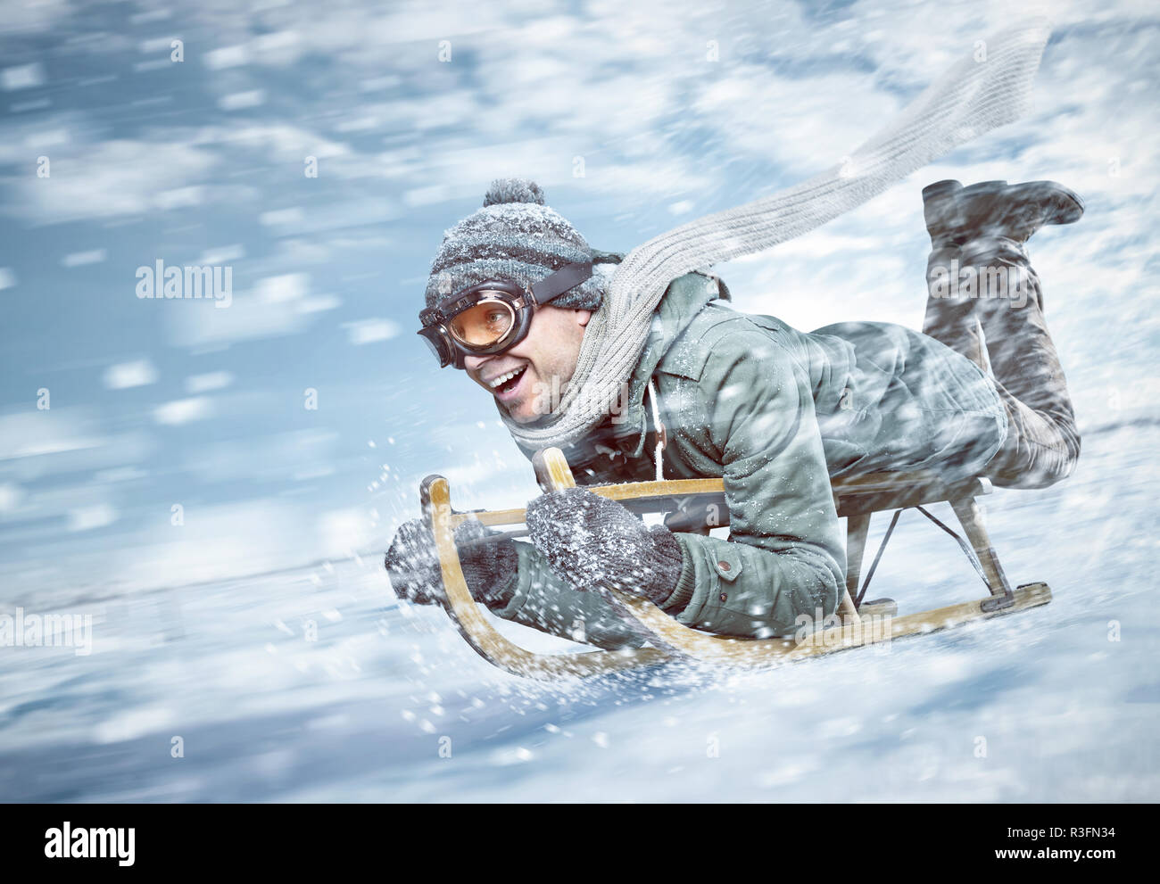 Cheerful man sledging down a snowy slope in full speed Stock Photo