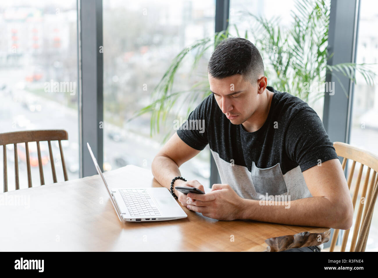 Freelancer work on netbook in modern coworking. Young man Typing on a smartphone,. Programmer at remote job. Successful people, businessman in comfortable cafe. High large Windows Stock Photo