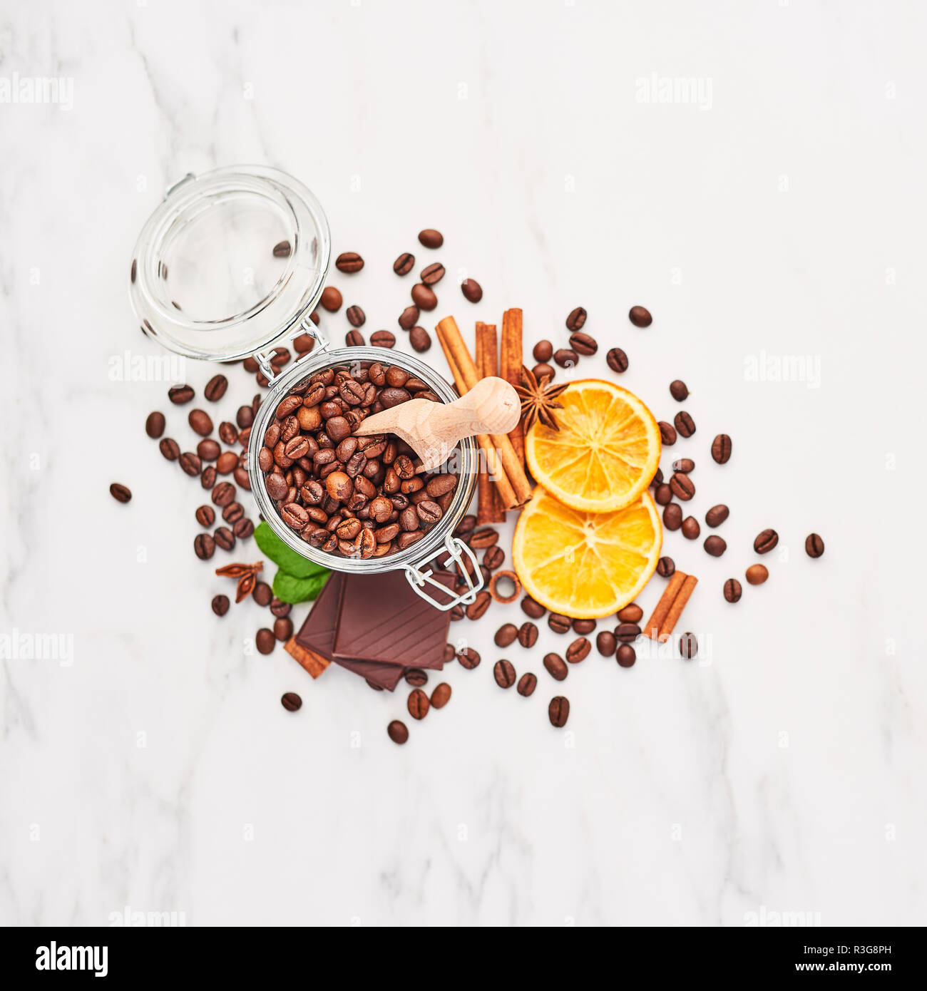 Coffee in a glass jar with beans, chocolate, dried oranges, anis and cinnamon sticks on white marble background. Concept of coffee with different spic Stock Photo