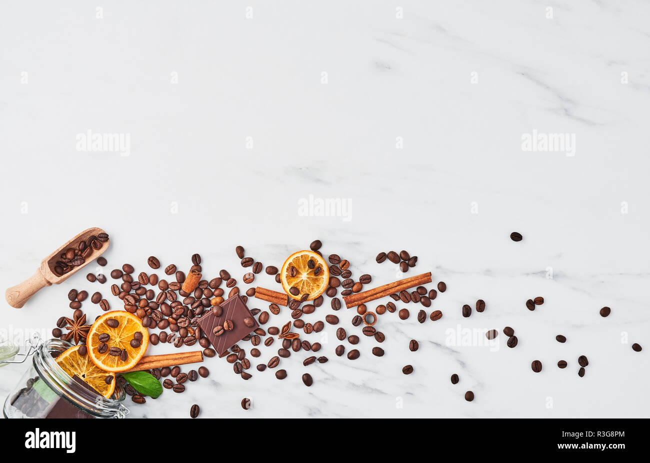 Coffee in glass jar with beans, chocolate, dried oranges, anis and cinnamon sticks on white marble background. Concept of coffee with different spices Stock Photo