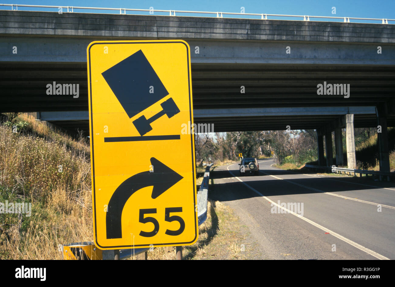 A ROAD SIGN WARNS DRIVERS TO REDUCE SPEED AS A BEND IN THE ROAD APPROACHES (ILLUSTRATED BY TRUCK TIPPING OVER) NEW SOUTH WALES, AUSTRALIA Stock Photo