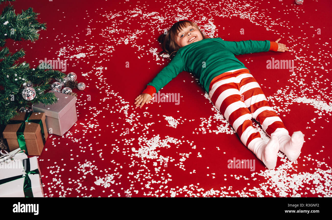 Happy little girl lying on floor beside a christmas tree. Kid having ...