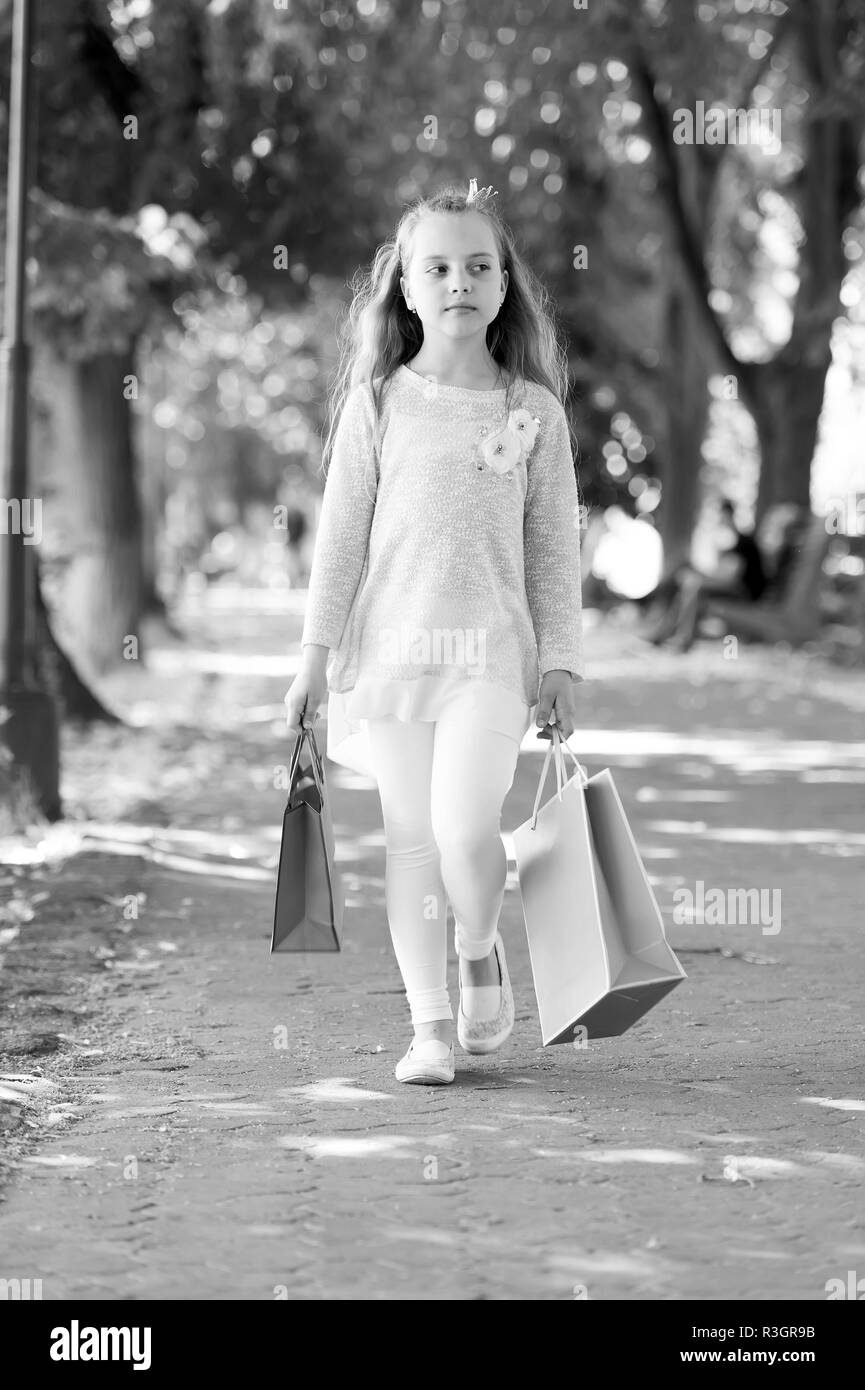 Kid shopper in fashion clothes outdoor. Child with paper bags in summer. Little princess with crown on long blond hair. Shopping on sale and purchase. Stock Photo