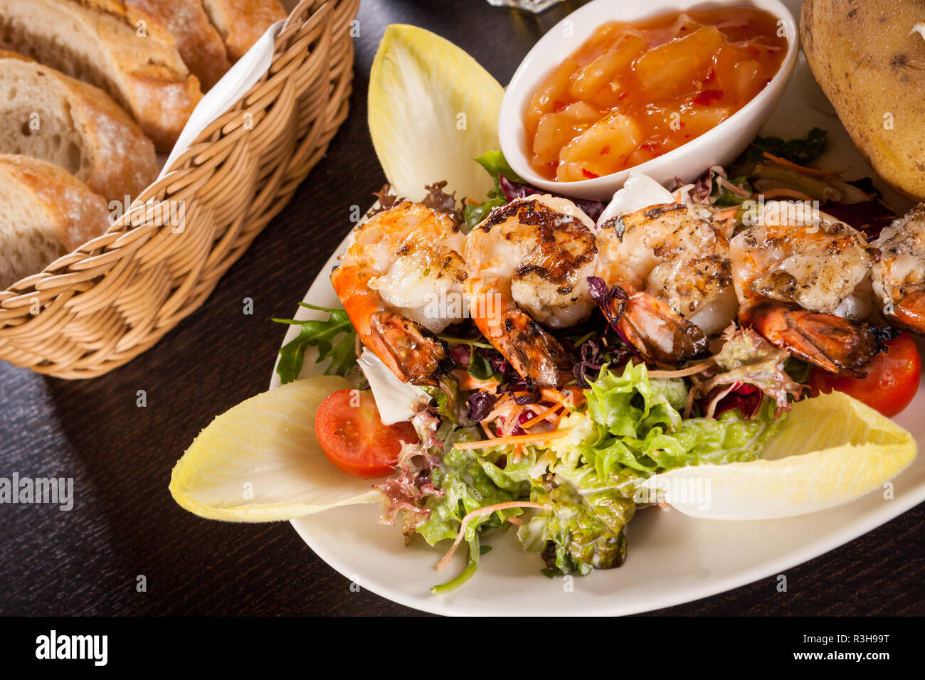 fried prawns on skewers with dipping sauce on mixed salad and baked potato Stock Photo