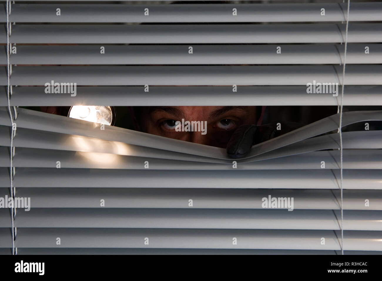 burglar with a flashlight looking through a window Stock Photo