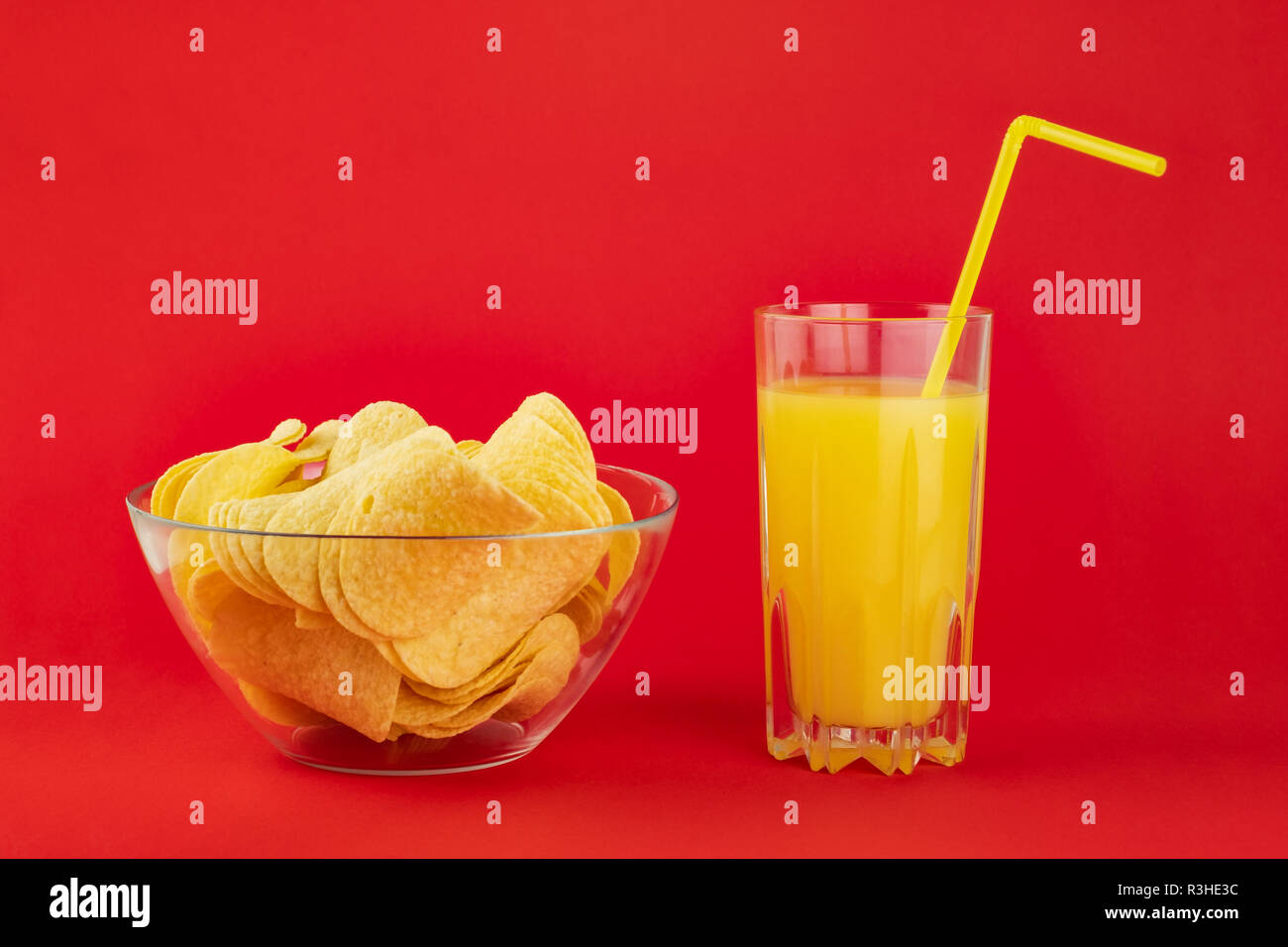 Bowl of potato chips and glass of orange drink in bright red background. Minimalistic image of attention grabbing snacks and beverage in vivid colors Stock Photo