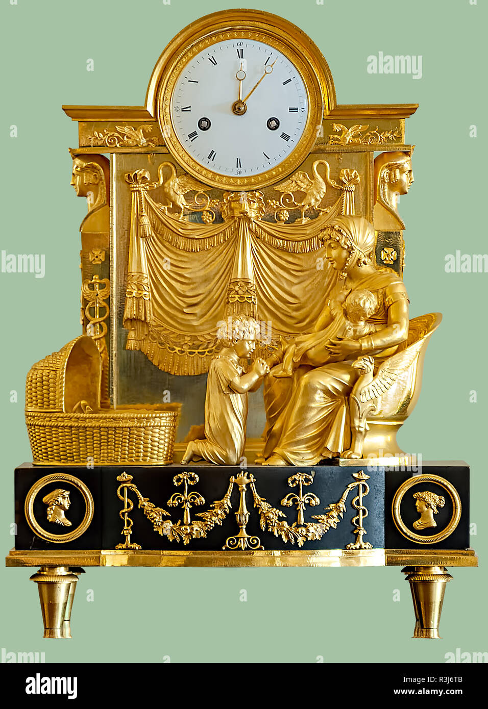 Antique mantel clock with golden statuettes of a woman and children on isolated green background with clipping path. Stock Photo