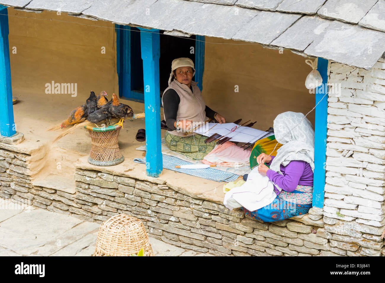 Two aged Nepalese women sitting in the doorway and sewing, Dhampus Mountain village, Nepal Stock Photo