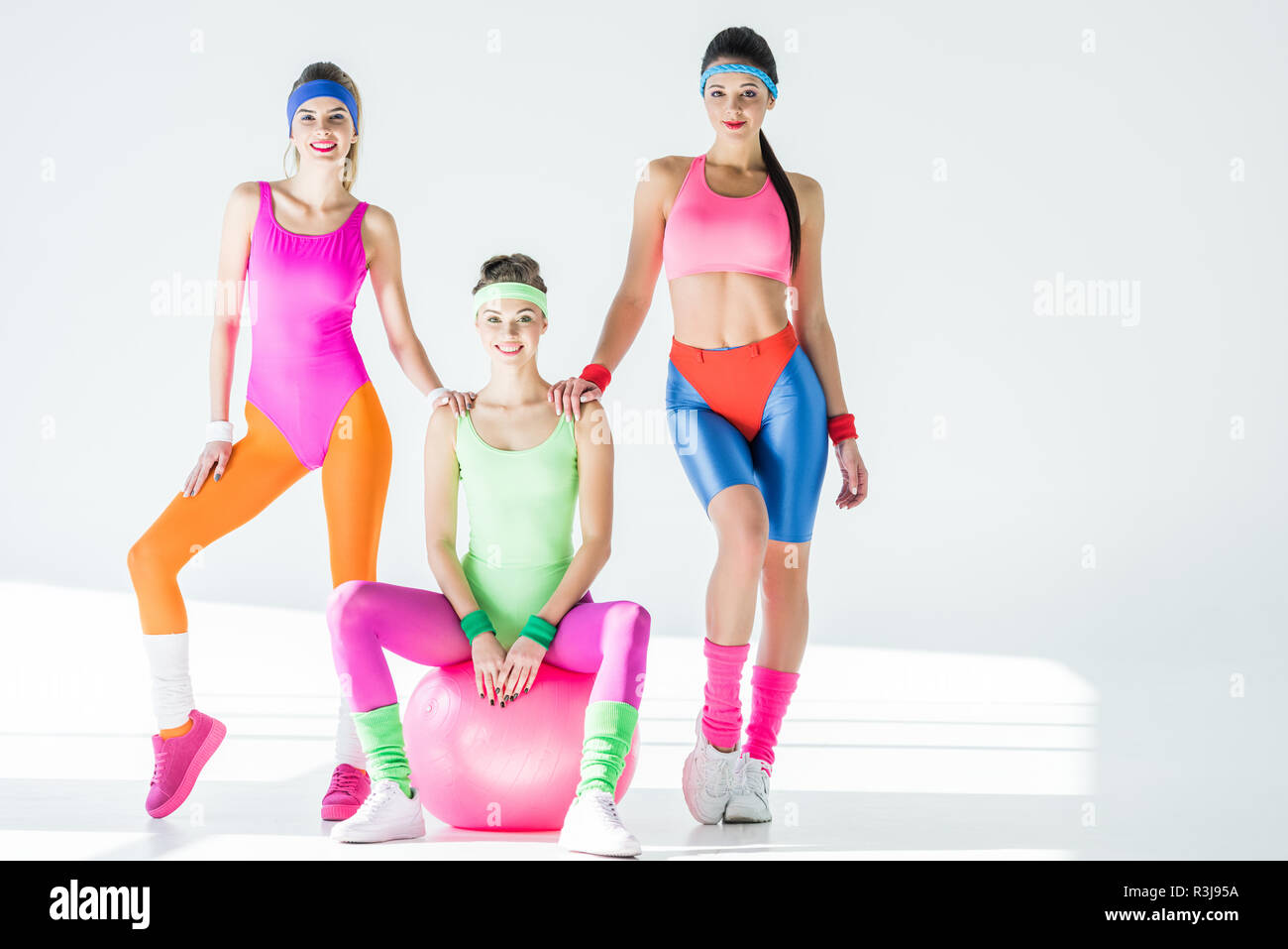 women in 80s style sportswear smiling at camera on grey Stock Photo -
