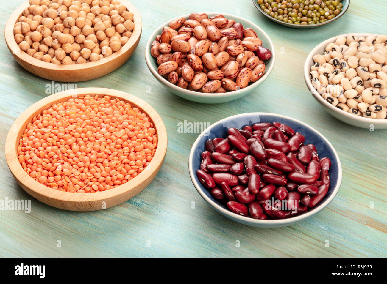 Various types of legumes on a teal background. Red kidney beans, lentil, chickpea, soybeans