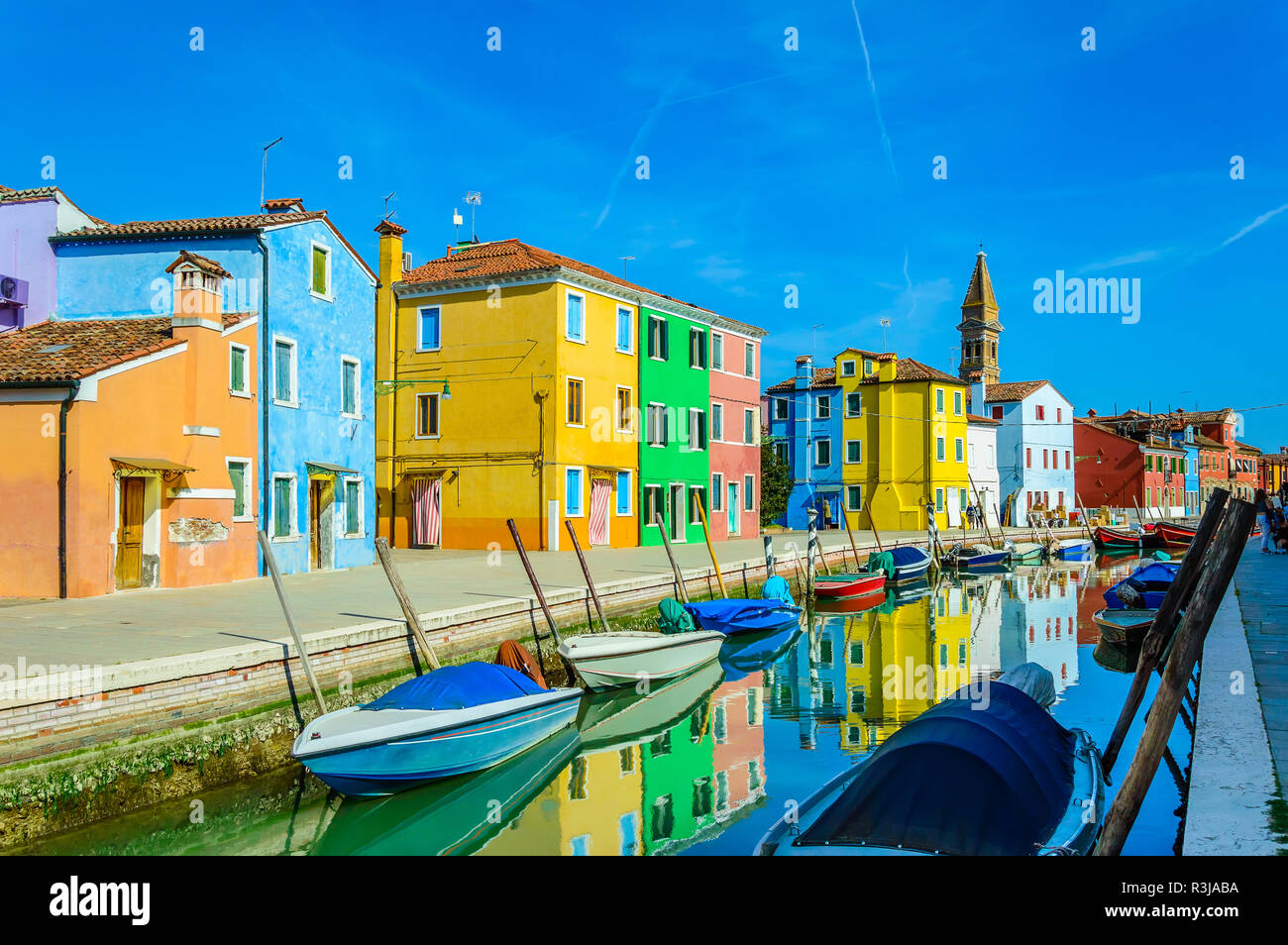 Colorful houses near canal on Burano island, Venice, Italy. Burano is famous for its lace work and brightly painted homes. Leaning campanile of San Ma Stock Photo