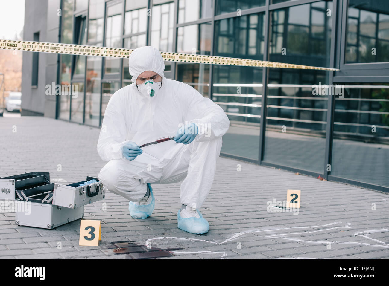male criminologist in protective suit and latex gloves explore the murder weapon at crime scene Stock Photo