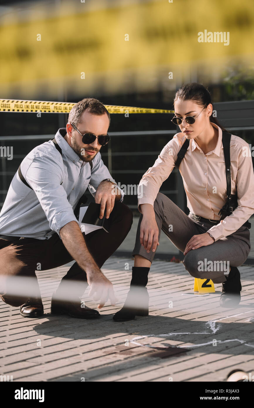 male and female detectives sitting and looking at chalk line at crime