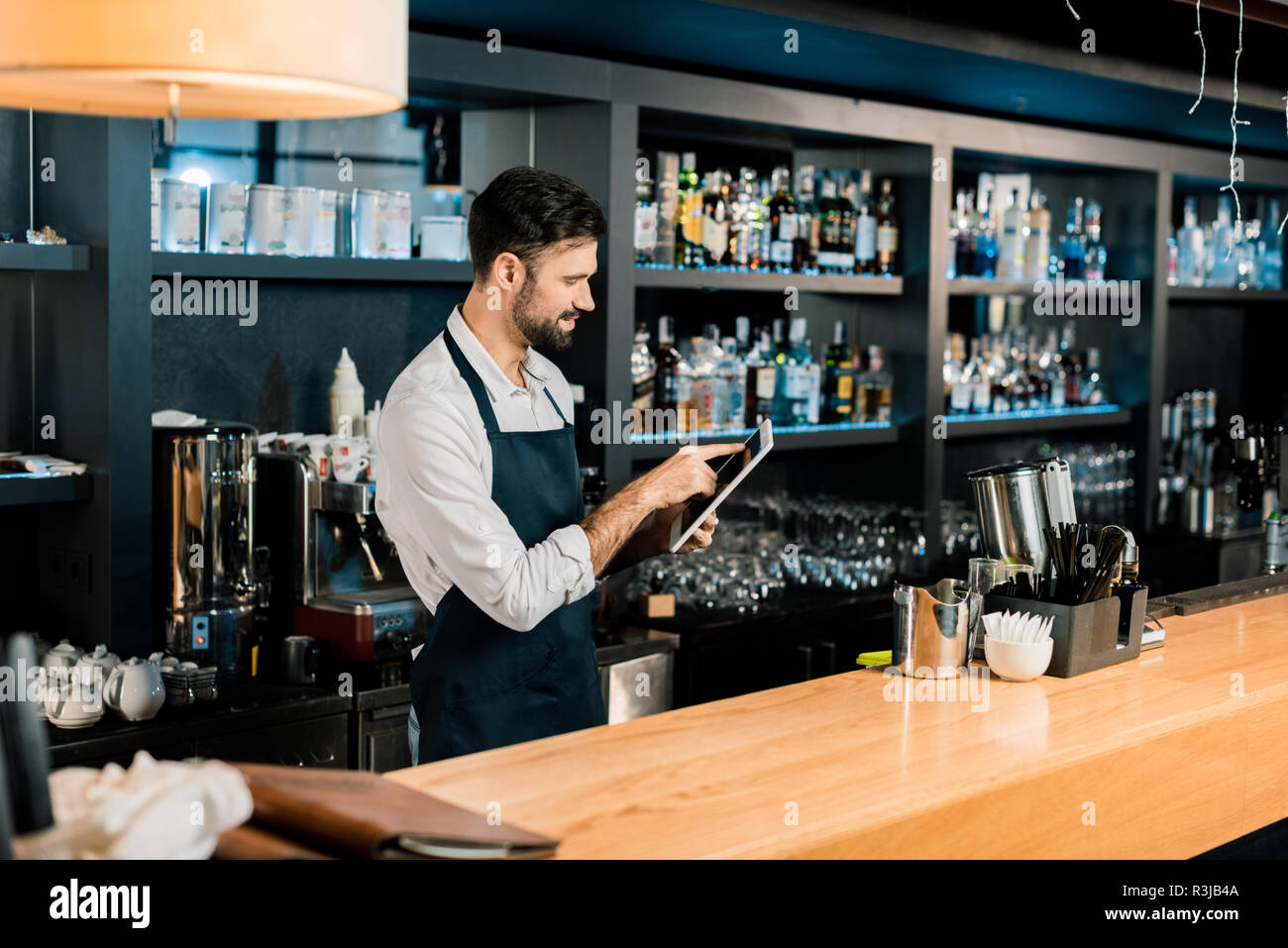 Barman standing in apron and typing on digital tablet Stock Photo