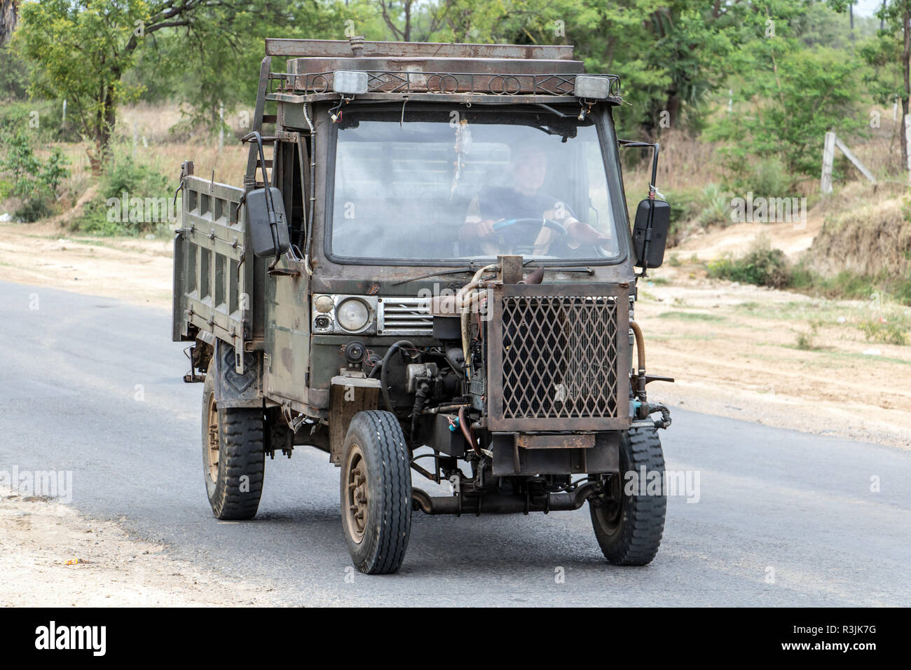 Chinese Manufactured tractor truck ride on road at countryside of Myanmar. Typical open-fronted battered lorry vehicle with air-cooled engine, Burma. Stock Photo
