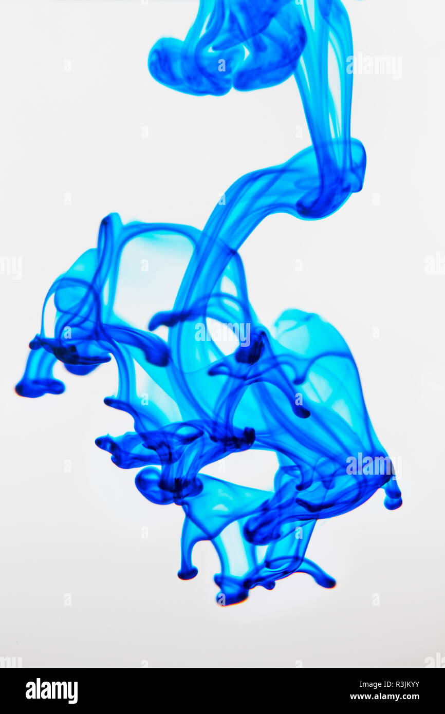 Food coloring dropped into glass of water and dispersing Stock Photo