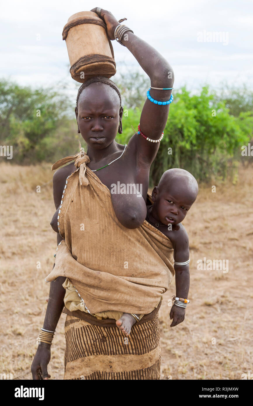 Africa, Ethiopia, Southern Omo Valley, Mursi Tribe. Mursi woman without her  lip plate inserted carrying her child and a wooden bucket Stock Photo -  Alamy