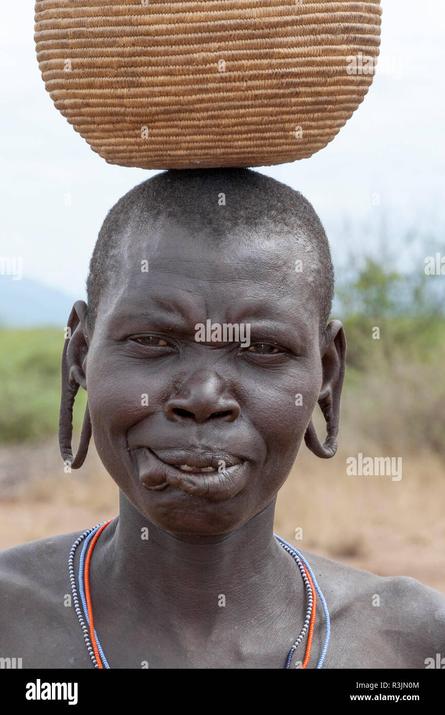 Africa, Ethiopia, Southern Omo Valley, Mursi Tribe. Portrait of an older woman without her lip plate inserted with a basket on her head. Stock Photo