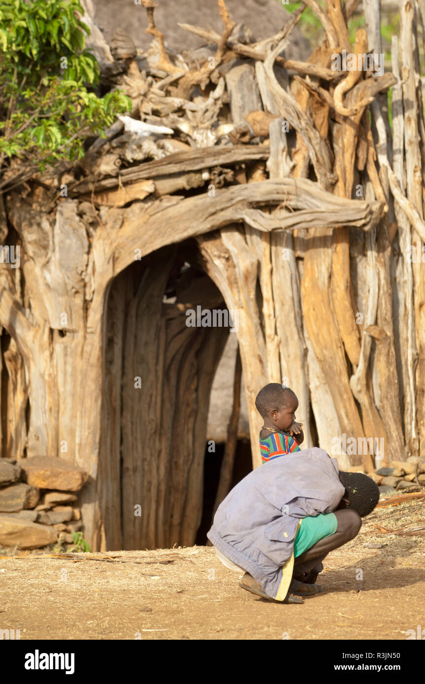 Africa, Ethiopia, Omo region, Konso. An older boy helps his younger brother with his shoes in front of Chief Kalla Gezalegn's wooden fenced compound. Stock Photo