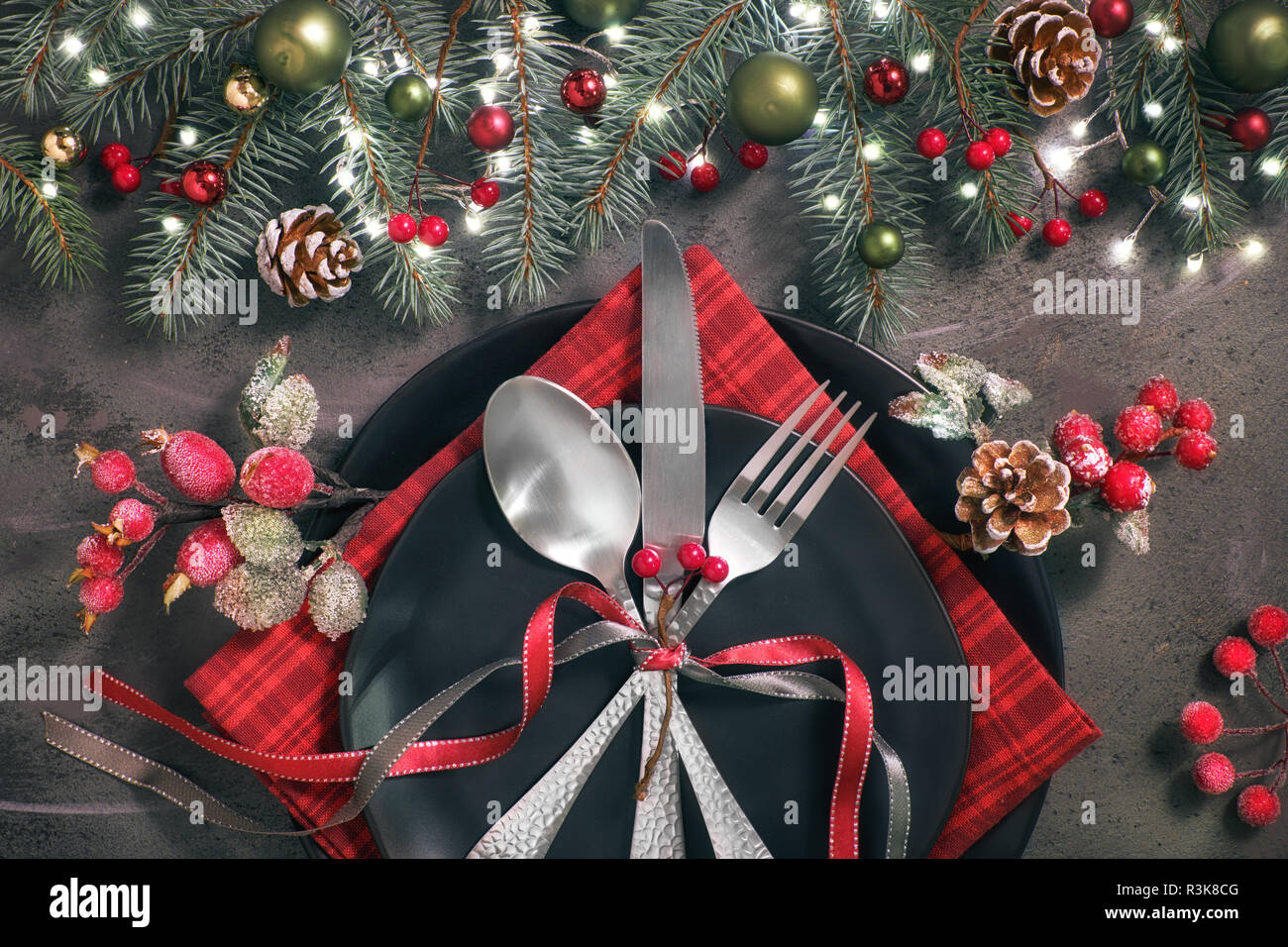 Christmas table setup on dark background. Flat lay with Xmas decorations in  green and red with frosted berries, trinkets, black plates and crockery  Stock Photo - Alamy