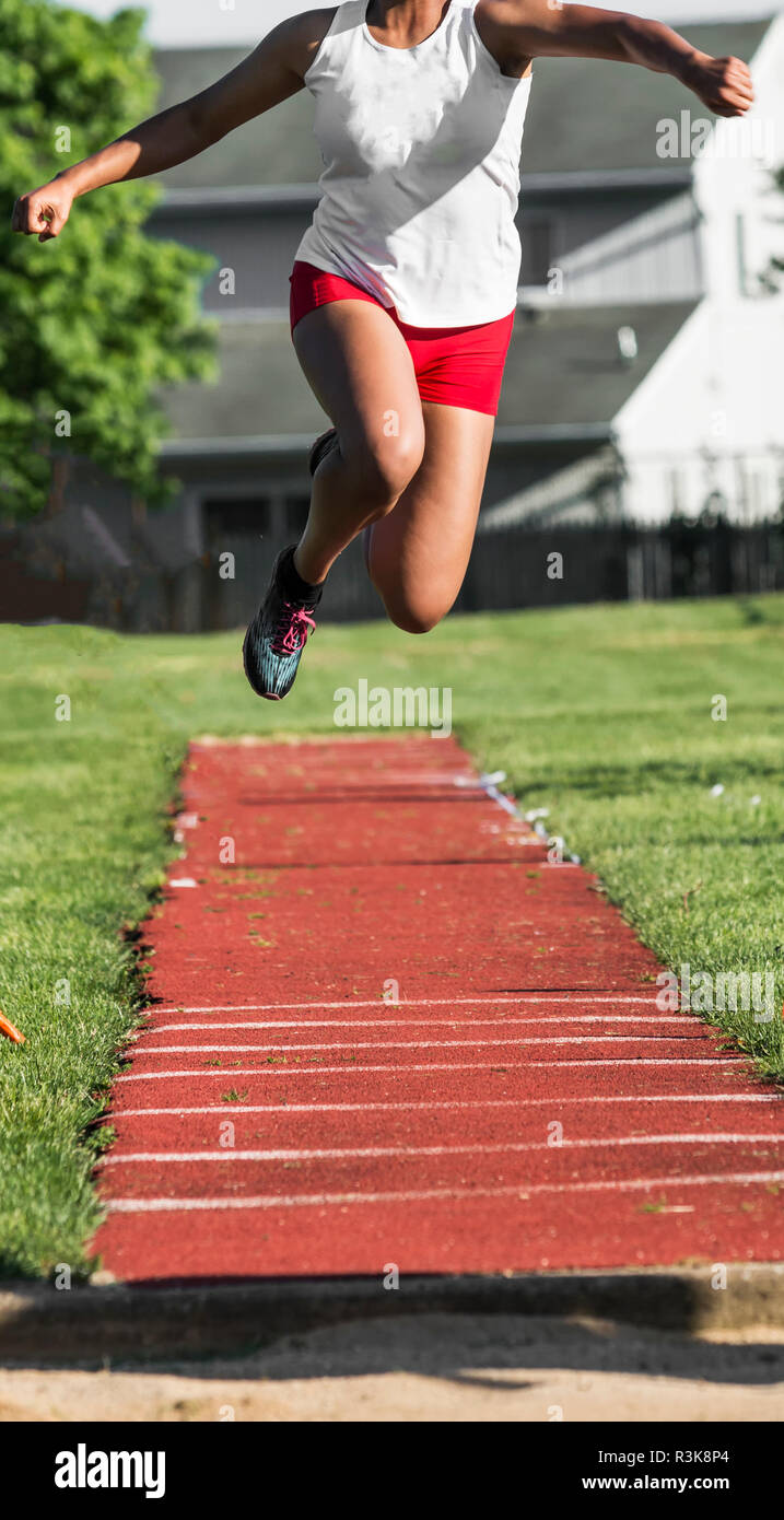 A high school female long jumper is high in the air heading toward the sand during a track and field competition outdoors. Stock Photo