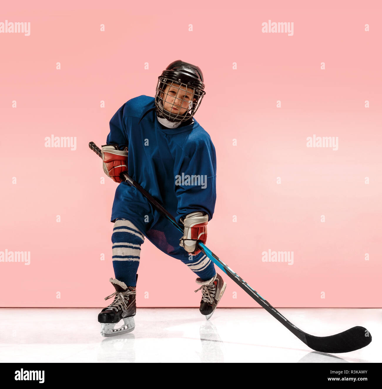 A hockey player in uniform with equipment over pink studio background