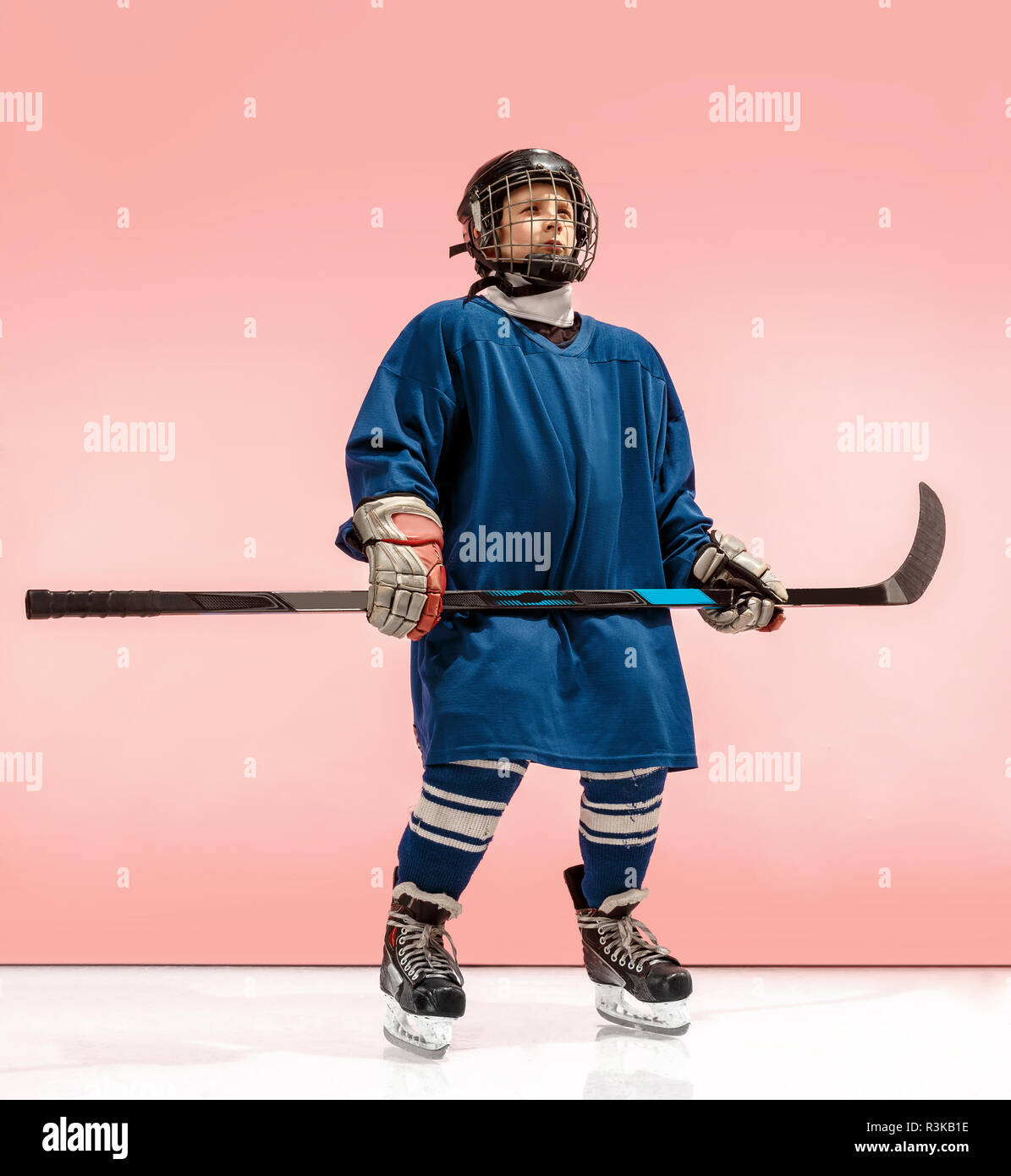 A hockey player in uniform with equipment over pink studio background