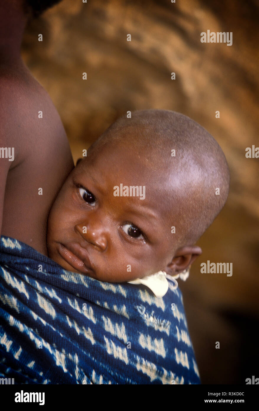 Africa, Mali, Koundou Gina village. Bottom of baby's feet show through the cloth carrier on the back of a teenage girl. Stock Photo