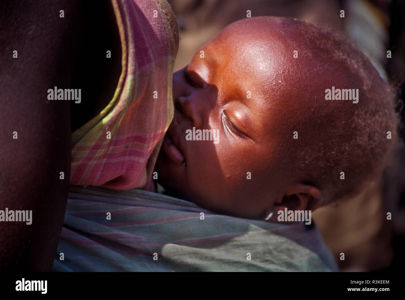 Nap time for a child nestled on mother's back in the Bedik tribe village called Damba or Dambakoi in remote Southeast Senegal, Africa. Stock Photo