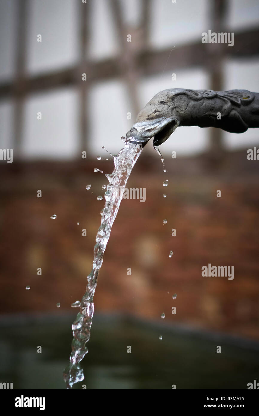Fresh water splashing out of an vintage tap in front of an old timbered house in the background Stock Photo