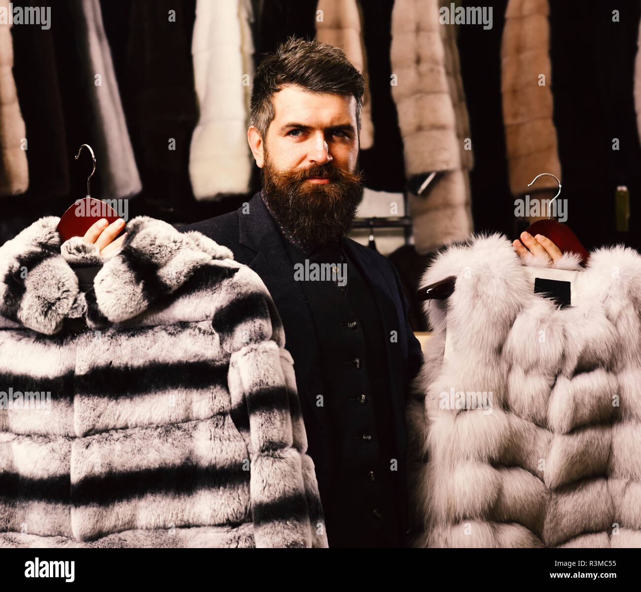 Man with beard and mustache in fur shop. Shop assistant holds grey sable and striped chinchilla fur coats. Masculinity and fashion concept. Guy with s Stock Photo Alamy