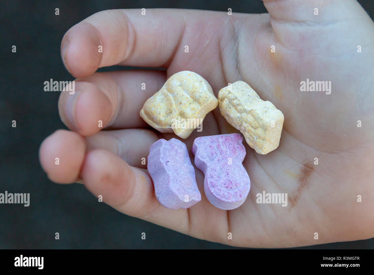 A close up view of a small child holding four animal shaped vitamins in