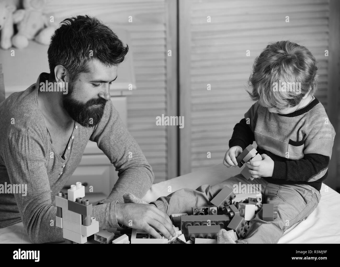 Dad and kid build of plastic blocks. Father and son with happy faces create colorful constructions with toy bricks. Man and boy play on wooden wall ba Stock Photo