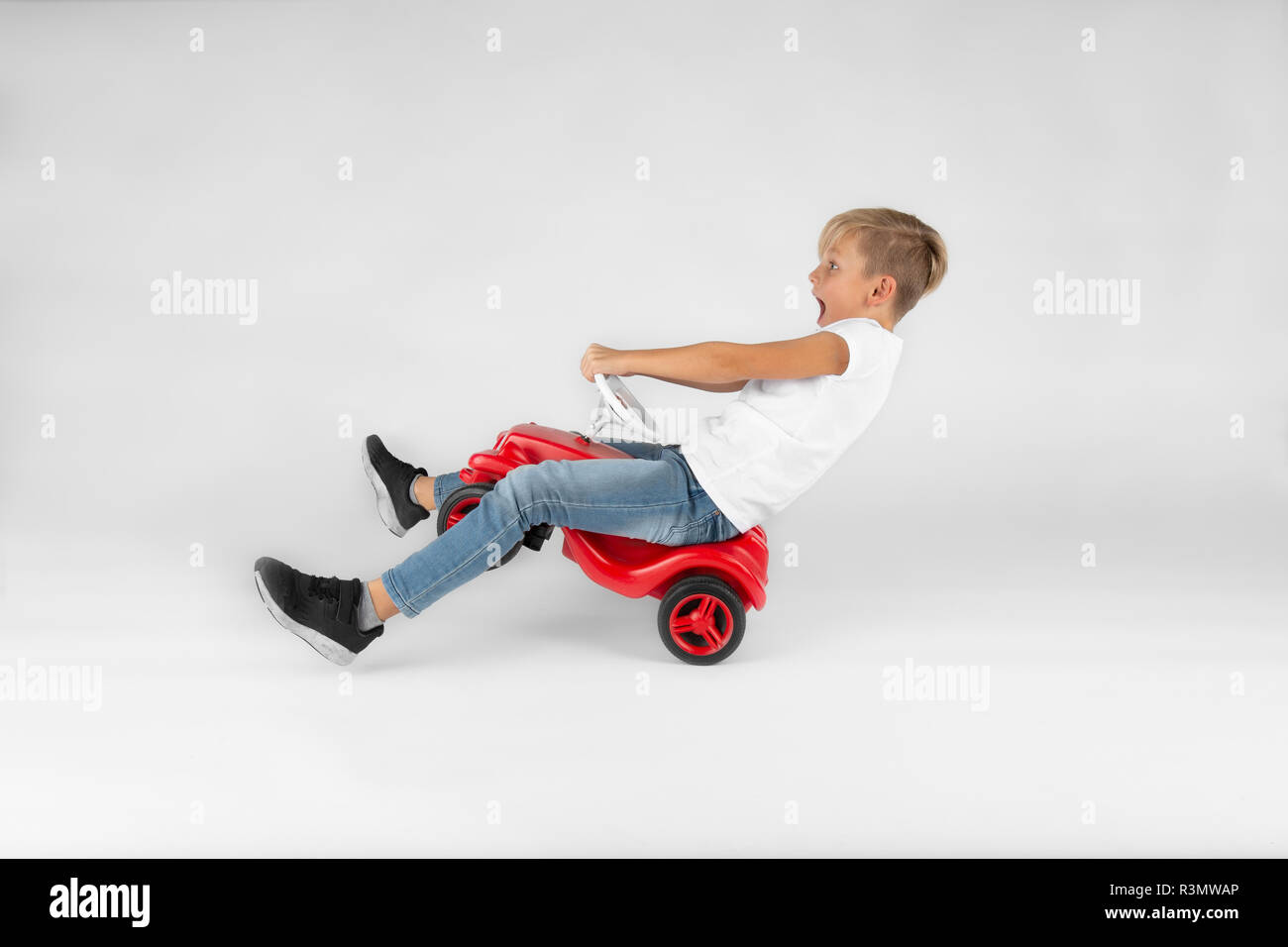 little blond boy is riding a toy vehicle very fast and is screaming Stock Photo