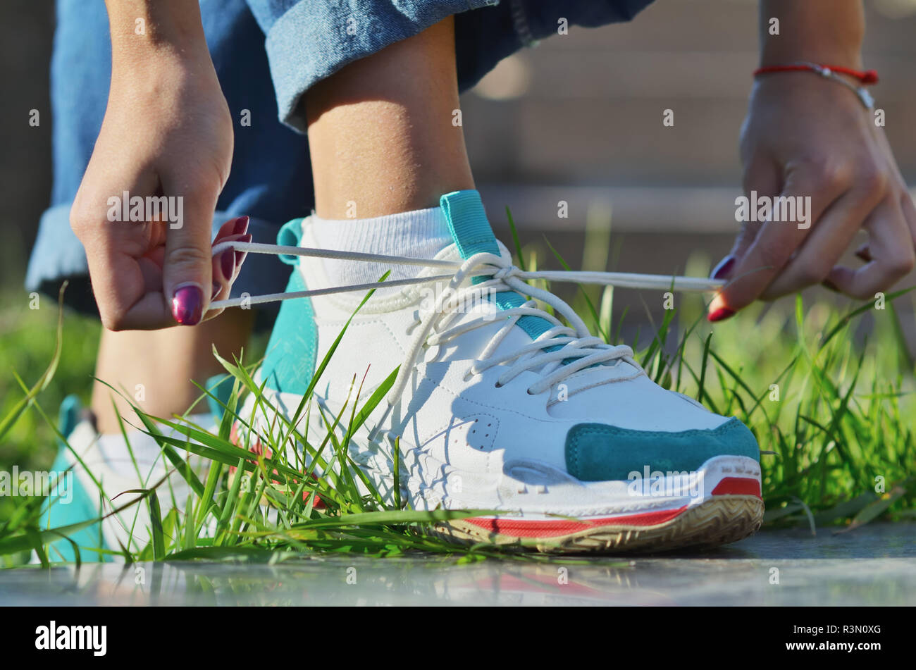 Young girl wearing jeans tying shoelaces on sneakers standing on green