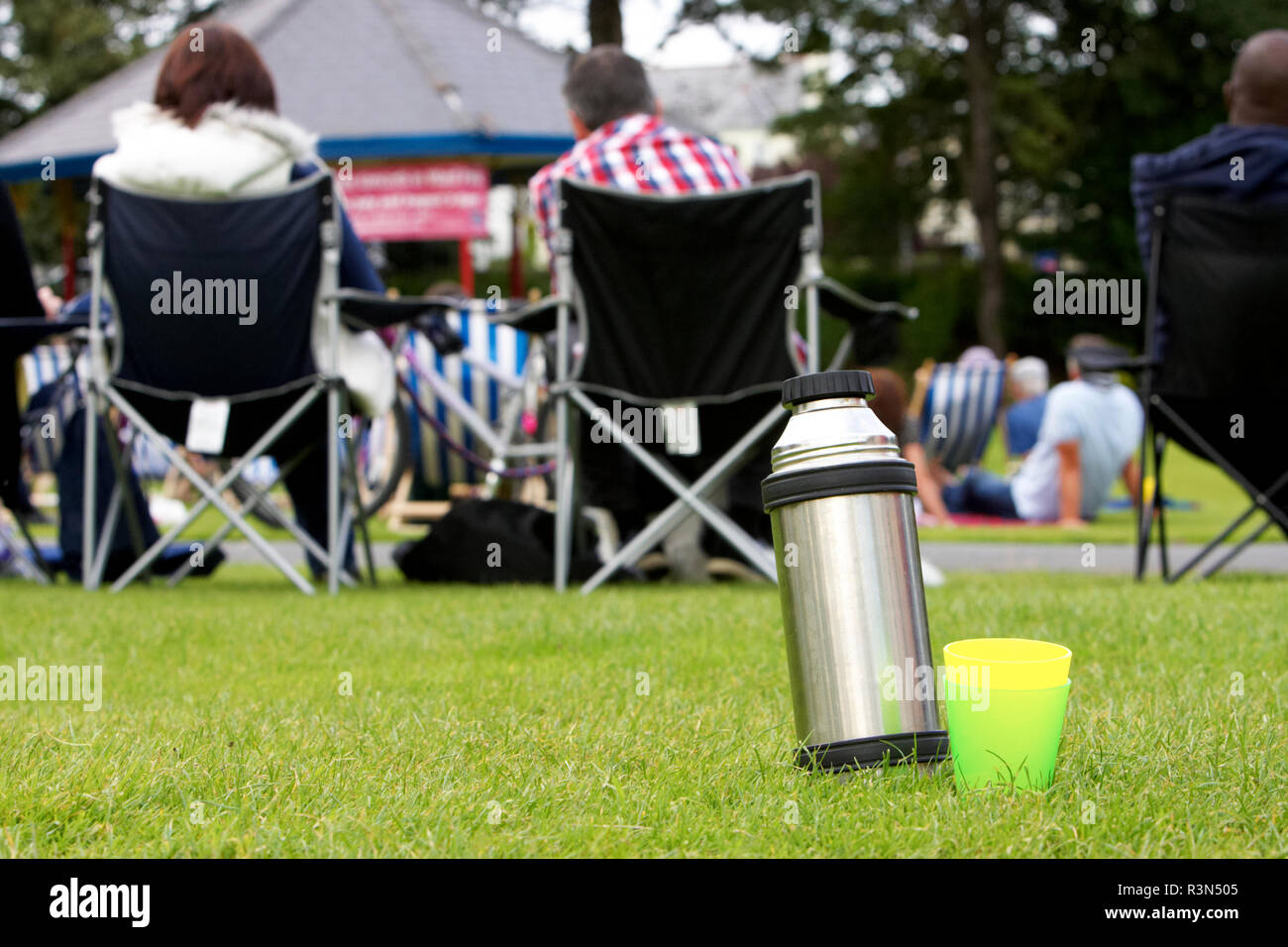 metal thermos flask on grass with two plastic cups outside during