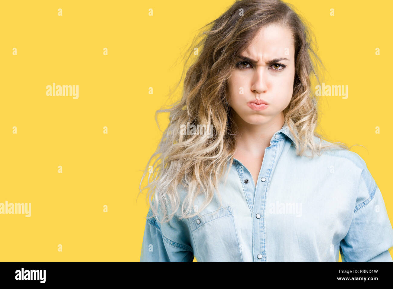 Beautiful young blonde woman over isolated background puffing cheeks with funny face. Mouth inflated with air, crazy expression. Stock Photo